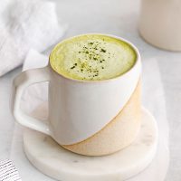 closeup photo of an earthy, two-toned mug full of match tea with milk with an extra sprinkle of green matcha powder on top