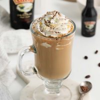 Image of a Baileys coffee topped with whipped cream and dusted with cocoa powder with coffee beans scattered in the background.