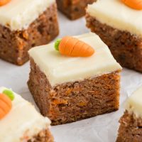 Image of several slices of carrot cake bars showing the thickness of the cake bars and all are topped with a creamy cream cheese frosting with a tiny candied carrot on top for decoration.