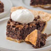Photo of a slice of chocolate cocoa pie with a golden crust and a dollop of whipped cream with a fork taking out a bite