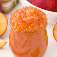 Photo of a jar full of homemade peach jam that looks delectable and ready to eat with an amazing peach hue.