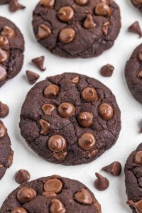 Close-up photo of a rich, dark banana cocoa cookie against a white background with chocolate chips scattered about.