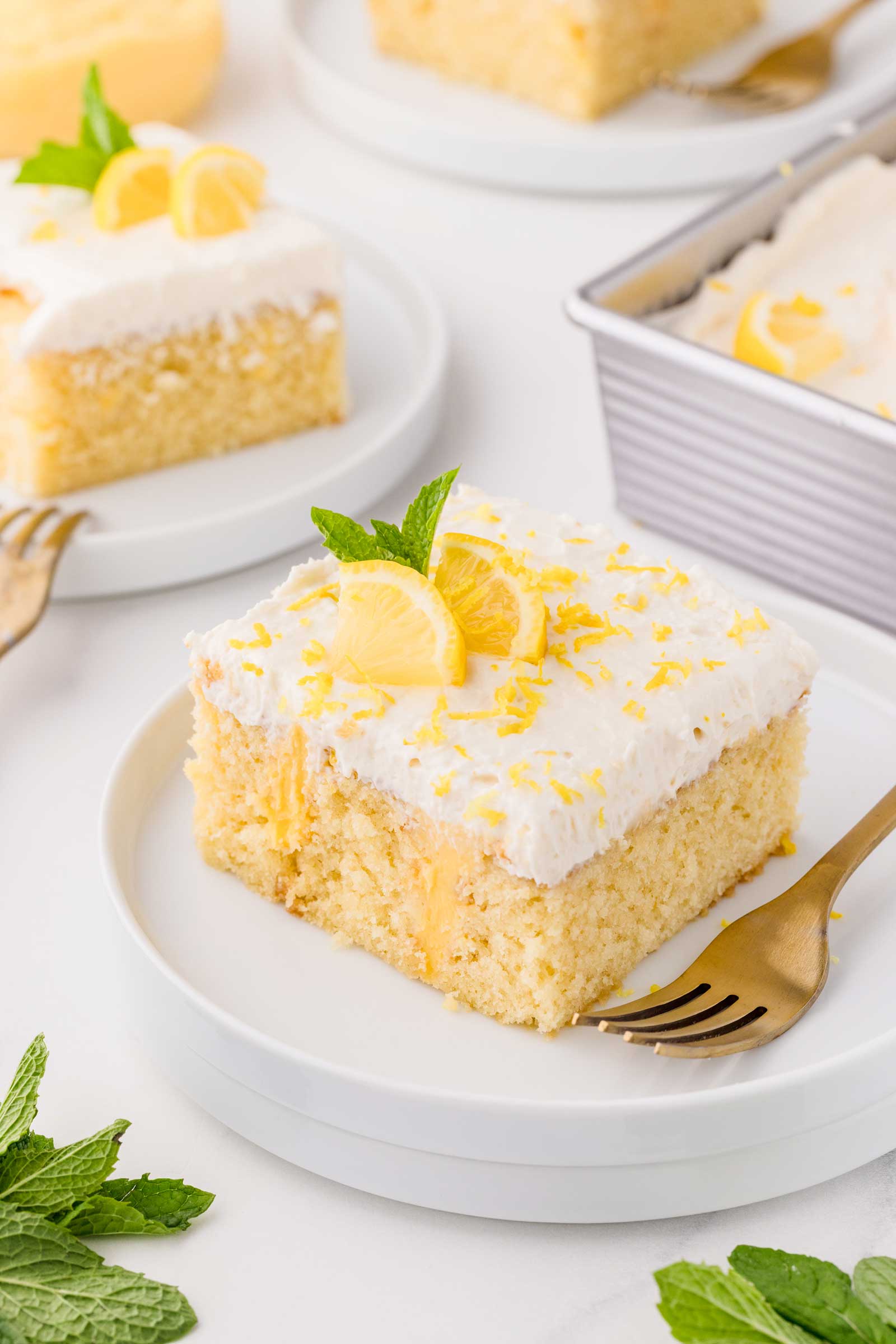 slice of lemon curd cake on white plate with mint and lemon wedge on top