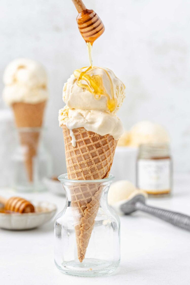 2 scoops of honey ice cream in an ice cream cone being drizzled with honey