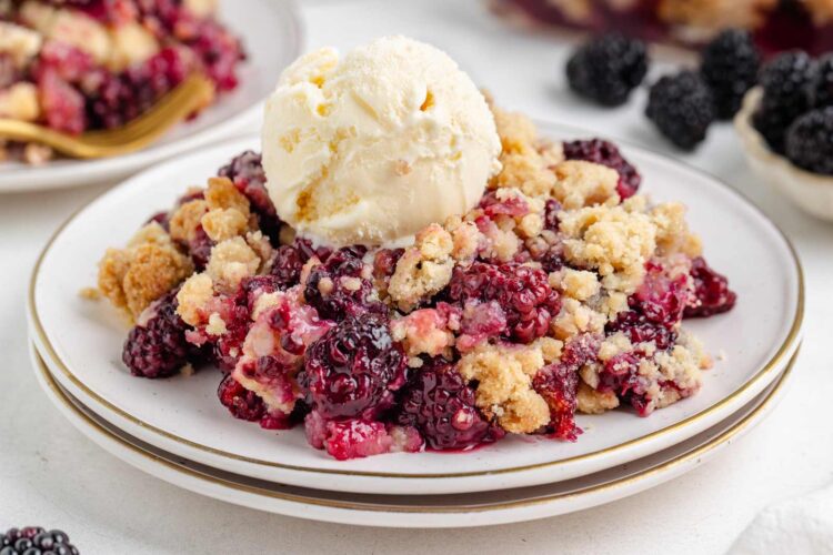 blackberry crumble on a white plate with a scoop of vanilla ice cream on top and another plate of crumble in background