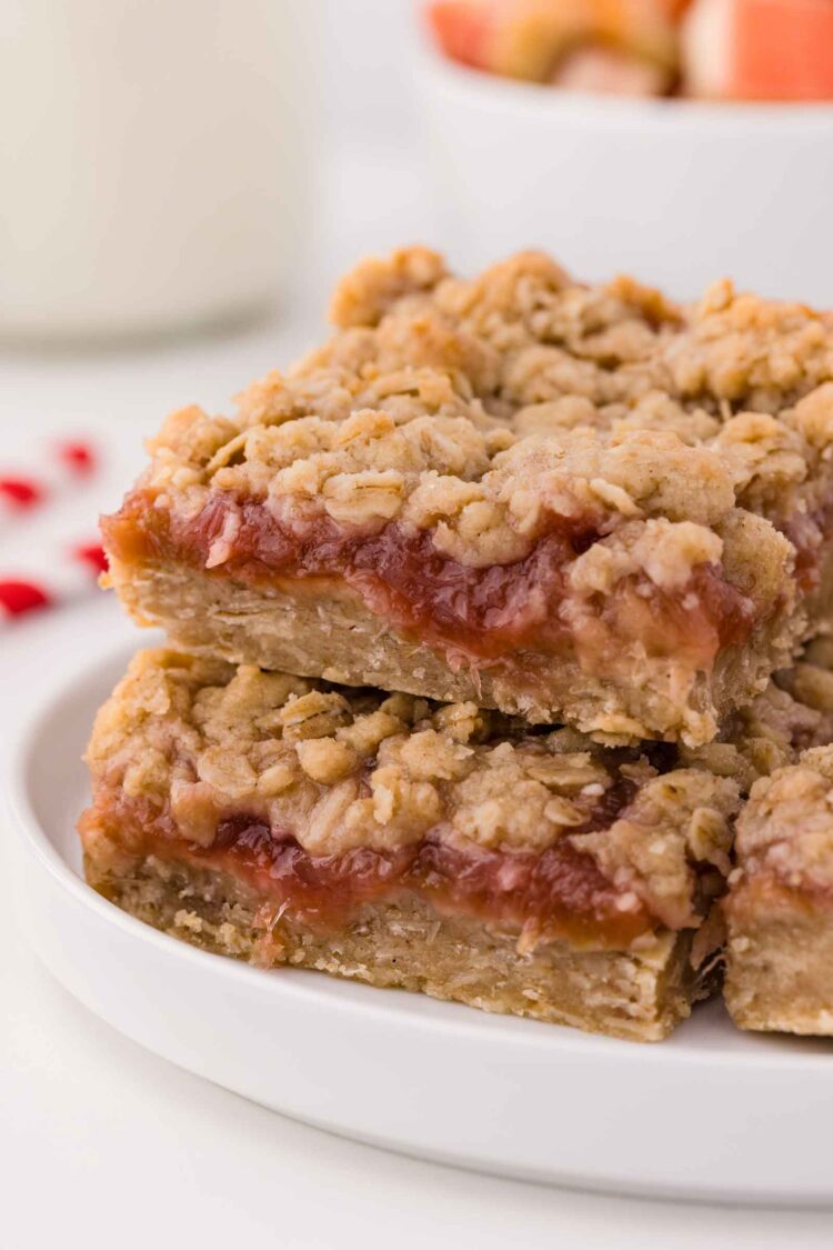 rhubarb bars on a white plate with more rhubarb in background