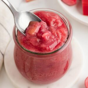 close-up of rhubarb compote in a small glass jar on a white table