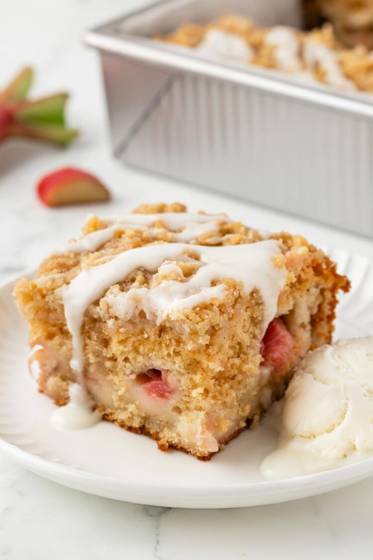 slice of rhubarb cake on a white plate with ice cream on the side