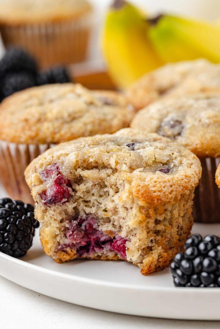 inside shot of a banana blackberry muffin on a white plate with blackberries on either side