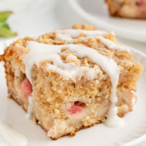 slice of rhubarb cake on a white plate with icing falling down the sides
