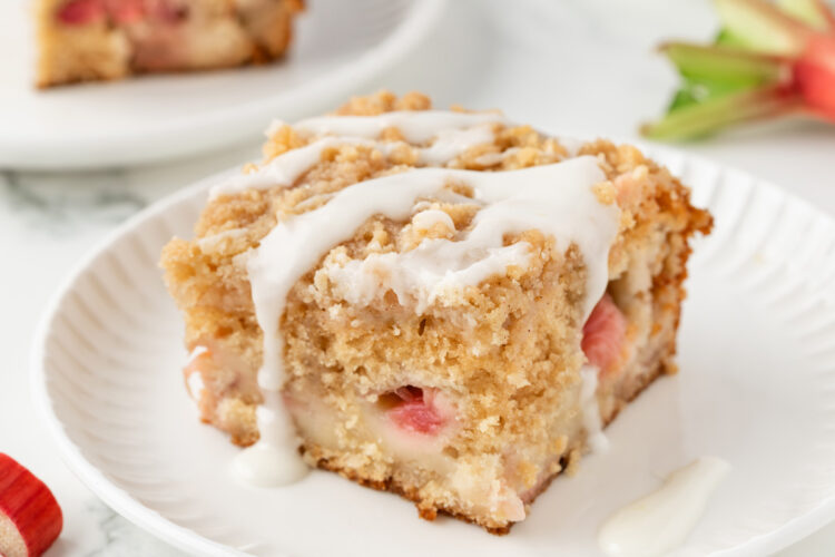 slice of rhubarb cake on a white plate on a white table with another slice in the background
