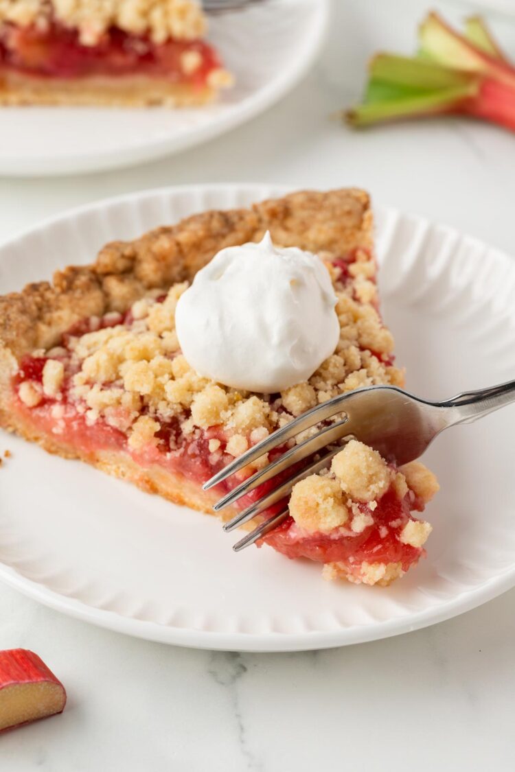 close-up of a slice of rhubarb tart on a white table with a fork digging into it
