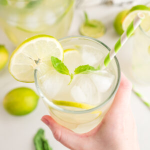 hand holding a glass of basil limeade with limes in background
