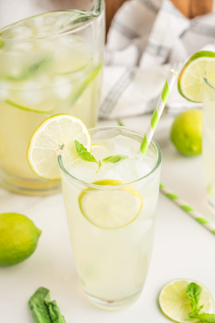 glass of basil limeade on white table with a pitcher in the background