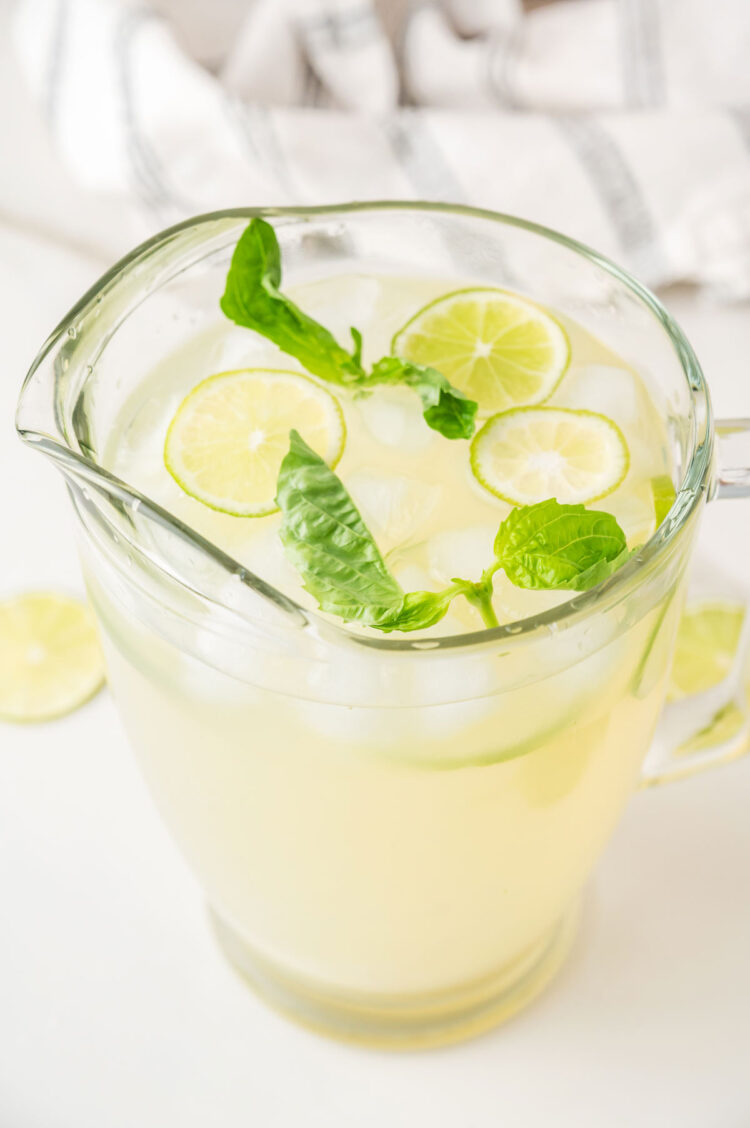 pitcher of basil limeade on a white table with ice and basil leaves