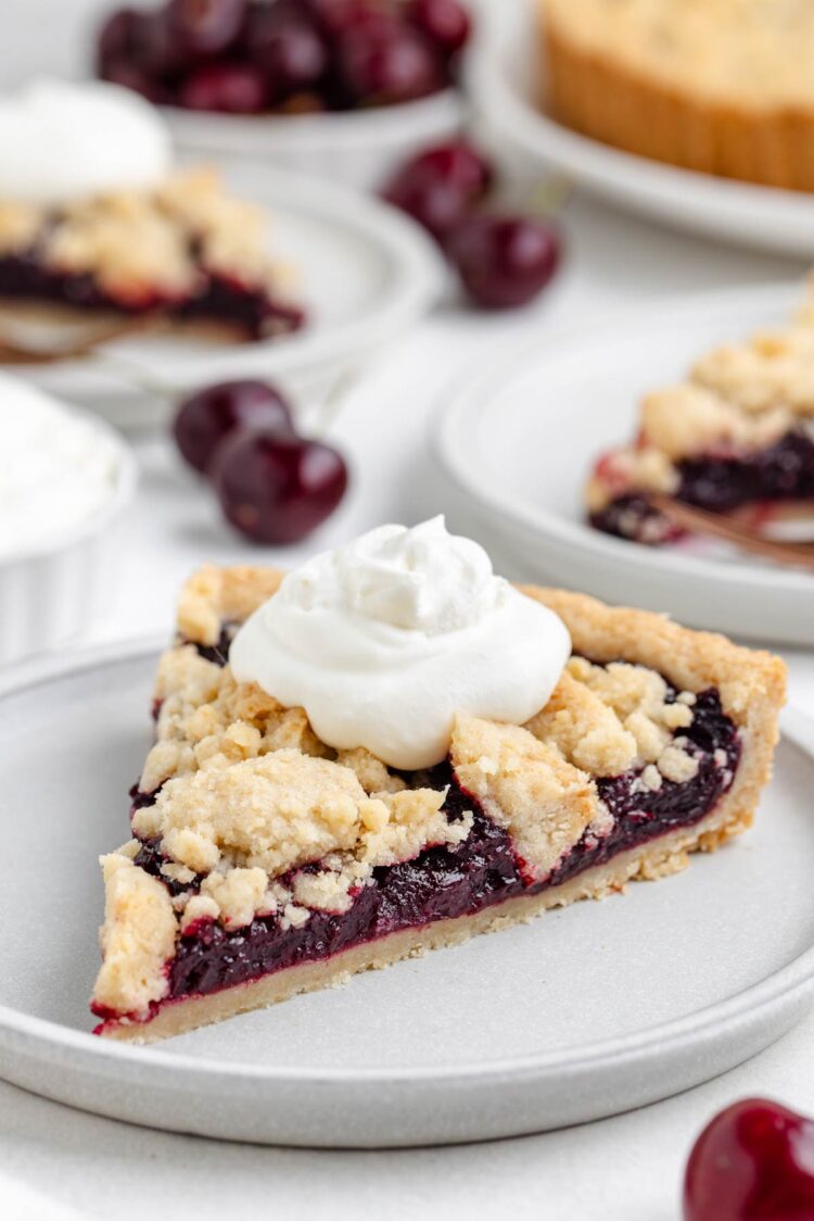 slice of cherry tart with whipped cream on top with more cherries on top in background