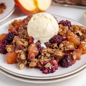 blackberry apple crumble on a white plate with ice cream on top