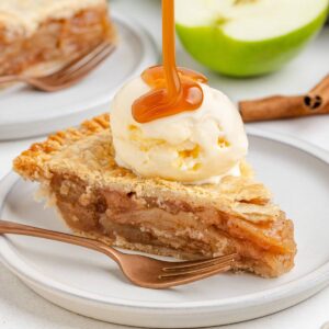 A slice of gluten-free apple pie topped with vanilla ice cream and caramel drizzle, served on a white plate with a fork.