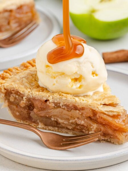 A slice of gluten-free apple pie topped with vanilla ice cream and caramel drizzle, served on a white plate with a fork.