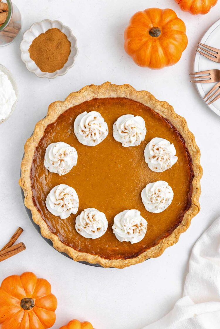Gluten-free pumpkin pie topped with whipped cream and surrounded by decorative pumpkins and spices.