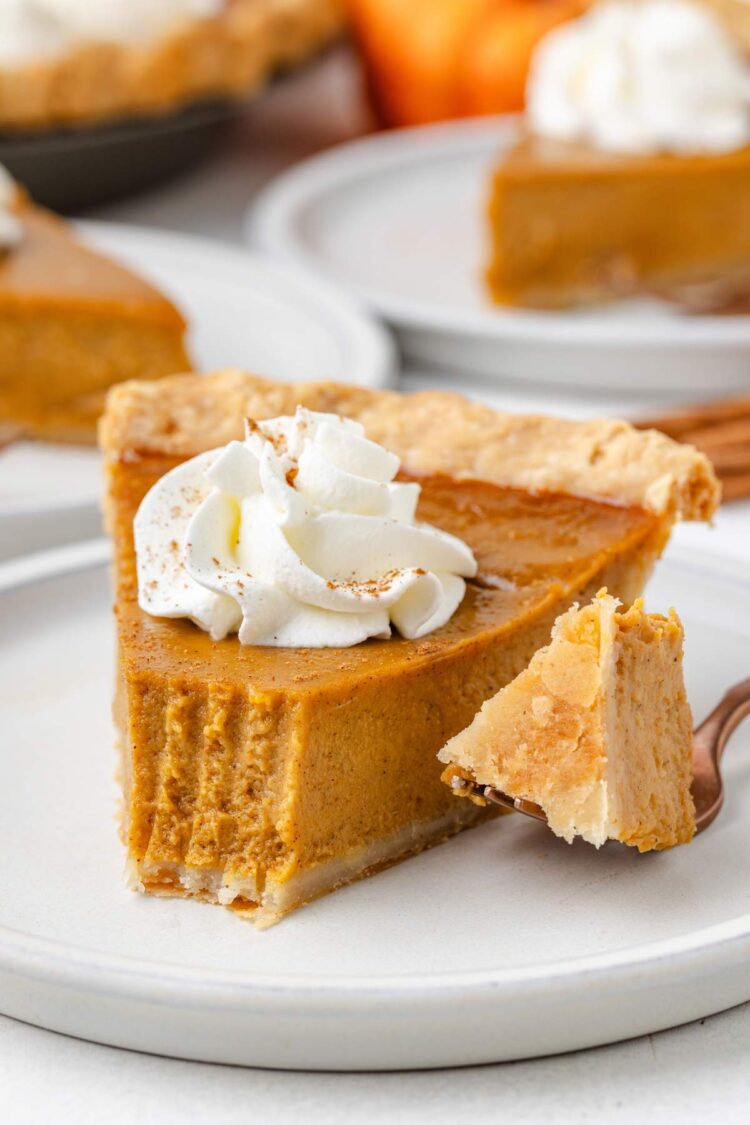 A slice of gluten-free pumpkin pie topped with whipped cream, served on a plate with a fork beside it.