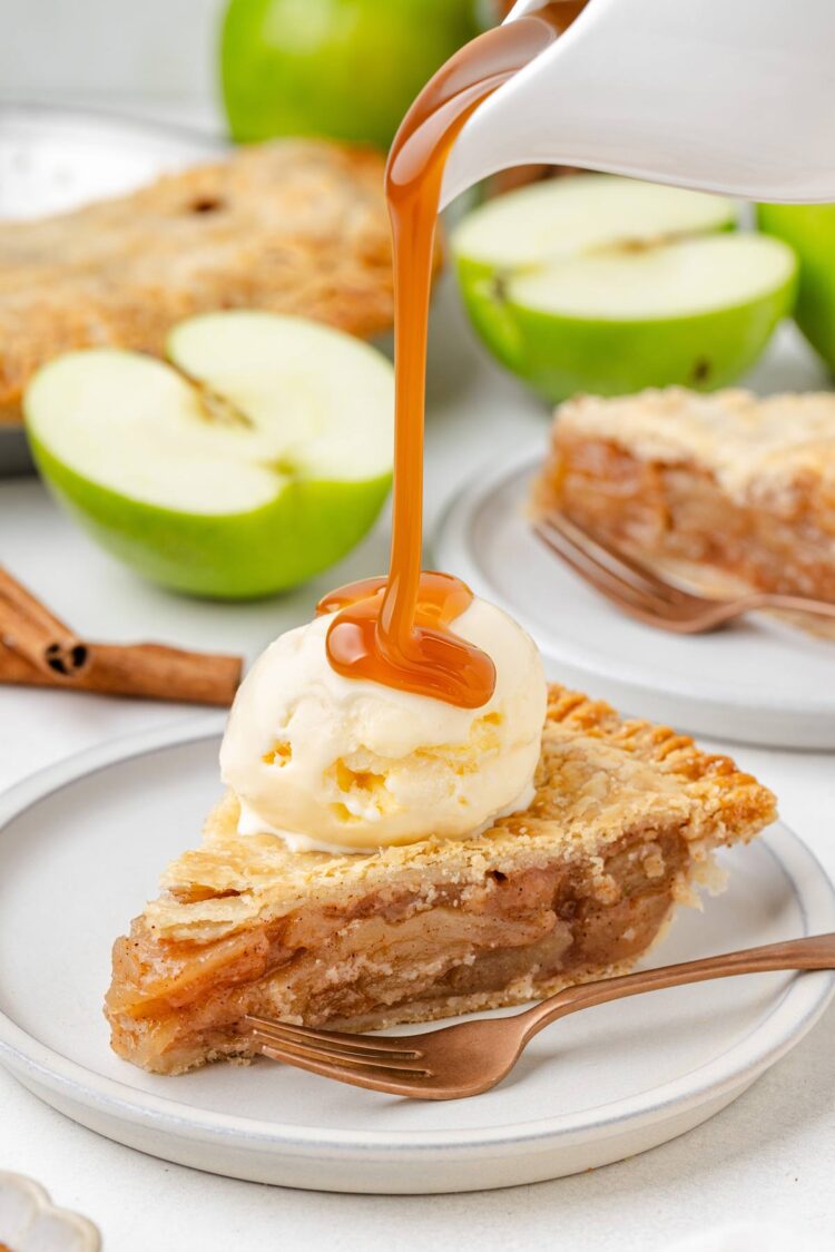 A slice of gluten-free apple pie topped with vanilla ice cream and caramel sauce, surrounded by green apple halves.