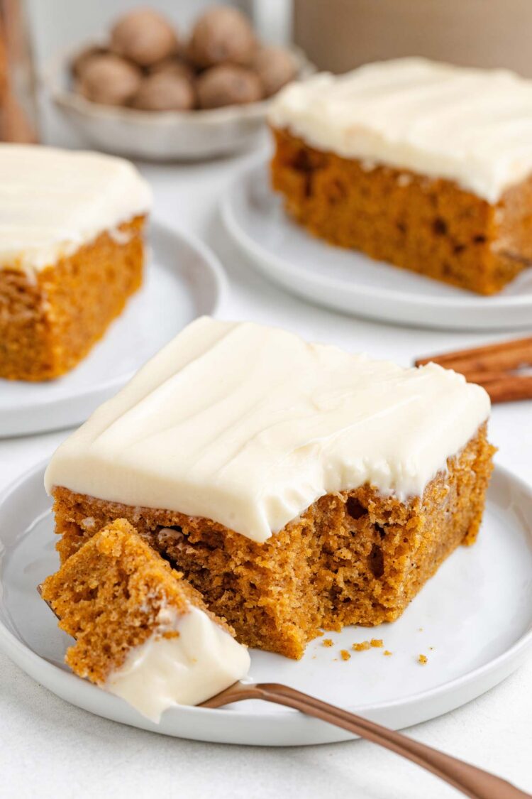 Moist sweet potato cake topped with creamy frosting, served on a white plate with a fork and cinnamon sticks in the background.