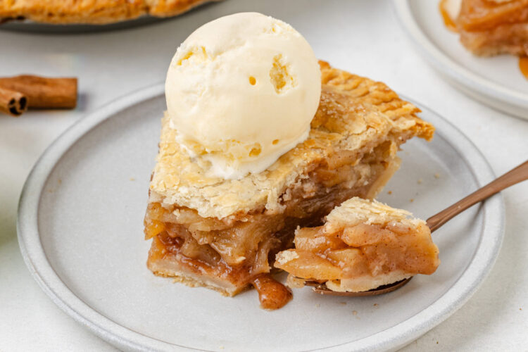 A slice of gluten-free apple pie topped with vanilla ice cream on a gray plate, with a forkful ready to serve.