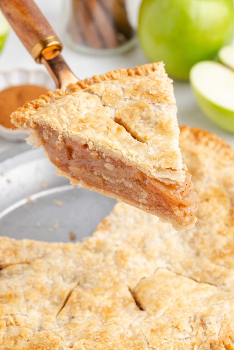 A slice of gluten-free apple pie is being lifted from the whole pie, showcasing its flaky crust and apple filling.