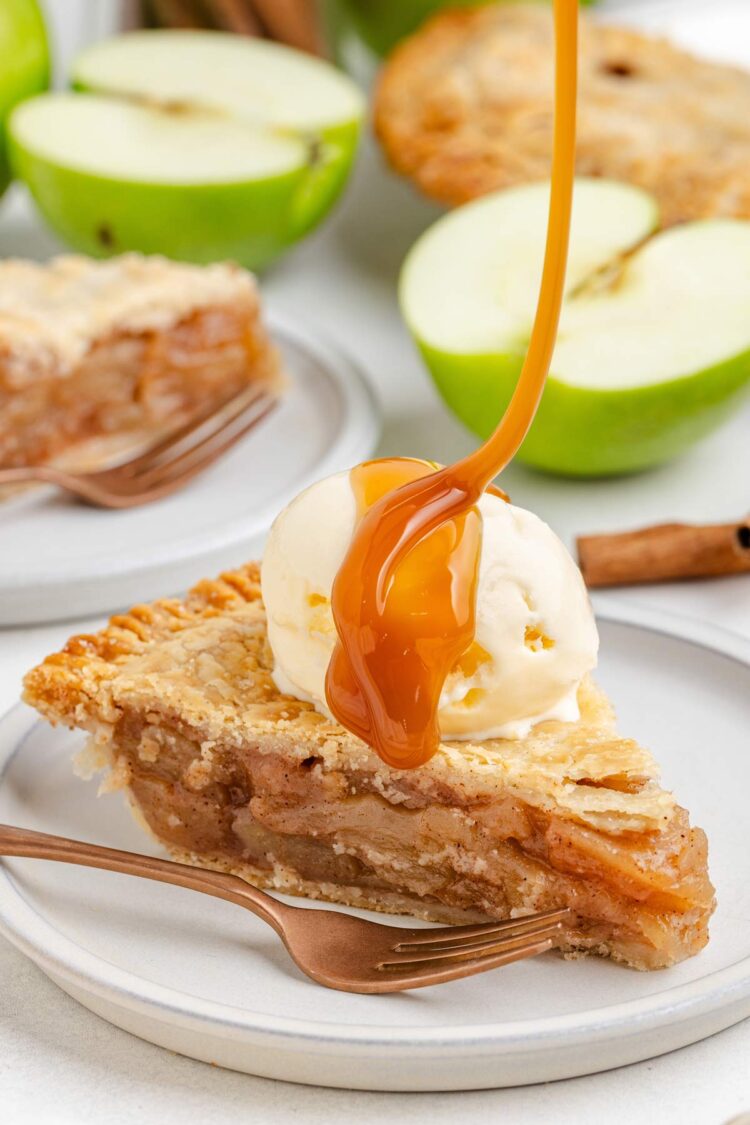 A slice of gluten-free apple pie topped with vanilla ice cream and caramel drizzle, surrounded by green apple halves.