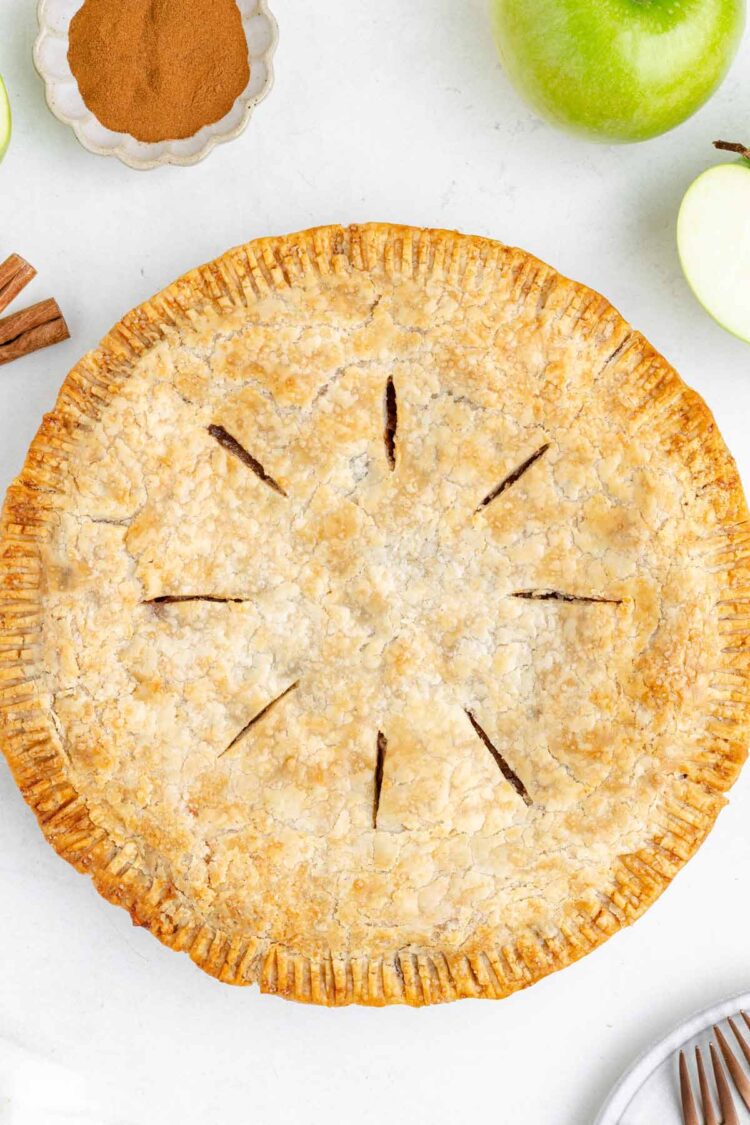 Golden-brown gluten-free apple pie with a flaky crust, surrounded by green apples and cinnamon.